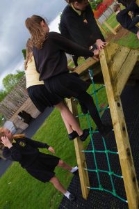 A wooden play ramp and net climber on a safety surface